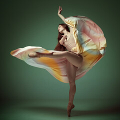 Young classical dancer wearing colorful flying dress dancing on fingertips over dark green background. Tender soul © Lustre Art Group 