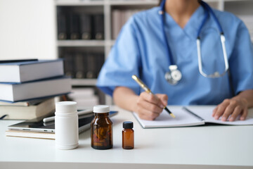 Close up view of young female doctor working in her office room with bottles of pills on her table.