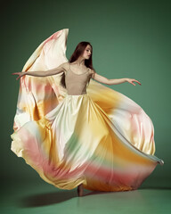 Young ballerina dancing elegant, grace movement with flying fabric over dark green studio background. Rainbow dress © Lustre Art Group 