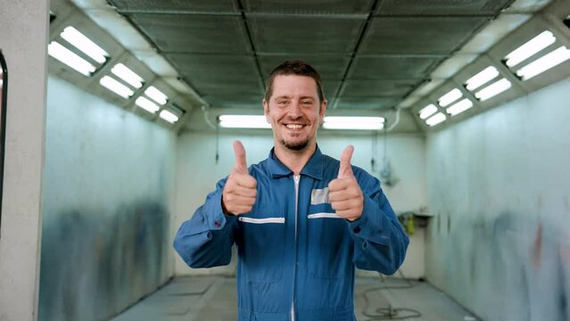 Slow Motion, Caucasian male mechanic standing in front of car painting room Raise both thumbs To demonstrate confidence in repairing the cars of customers who come to use the service.. in the garage
