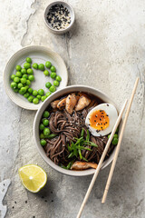 Asian soba noodle soup, with chicken, boiled egg, sesame seeds, green pea and green onion served with chopsticks. Top view, flat lay