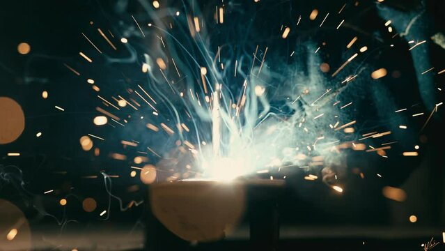 Close-up blacksmith welder in protective mask works with metal using a welding machine, bright sparks and flashes in super slow motion