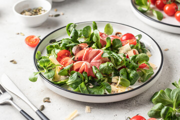 Fresh Green salad with ham or prosciutto, corn salad leaves, tomatoes and cheese. Healthy diet lunch on white marble background