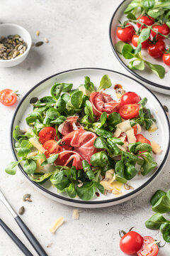 Green salad with ham or prosciutto, corn salad leaves, tomatoes and cheese. Healthy diet lunch on white marble background
