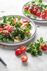 Green salad with ham or prosciutto, corn salad leaves, tomatoes and cheese. Healthy diet lunch on white marble background