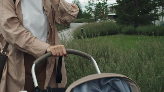 Dolly shot of young Caucasian woman recoding voice message on smart watch while walking with baby in stroller