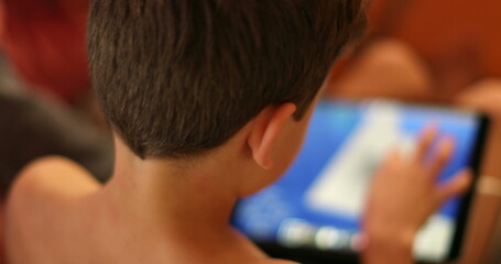 Young boy using tablet device tech. Back of Child perspective playing video-game