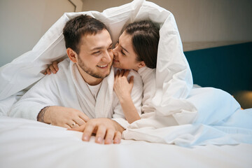 Husbands in love hugging and whispering under covers on large bed