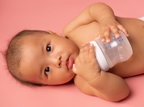 Adorable Little Baby Asian Girl Feel Good with milk bottle or feeding baby with milk infant hold bottle on Pink Background. ,baby 6 month old while drinks milk from a bottle