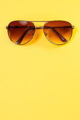 Close up of aviator style sunglasses with brown hues centered at top of a colorful bright yellow background making a fantastic summer backdrop with copy space.