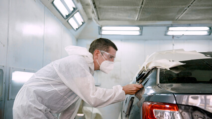 Caucasian Man mechanic, standing holding sheet thin steel sheet, inspecting car's paint, checking if car color customer's desired color matches or not spray equally or not, before assembling car.