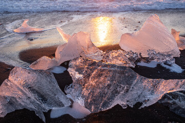 Pure Ice Shining on Black Volcanic Sand at Sunset. Icebergs from Glacier in Sun Rays. Clear Ice in Ocean Waves. Famous Tourist Location in North Europe Country. Travel Destination Diamond Beach..