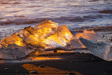 Pure Ice Shining on Black Volcanic Sand at Sunset. Icebergs from Glacier in Sun Rays. Clear Ice in Ocean Waves. Famous Tourist Location in North Europe Country. Travel Destination Diamond Beach..