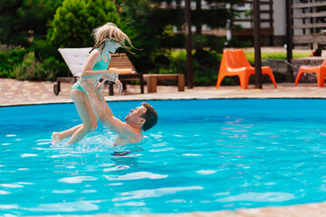 Naklejka premium Dad and daughter play in the pool. dad throws daughter in the air.