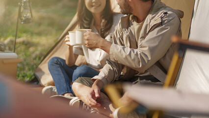 Asian couple drinking coffee enjoying camping outdoors in nature. Man traveler hands holding cup of coffee