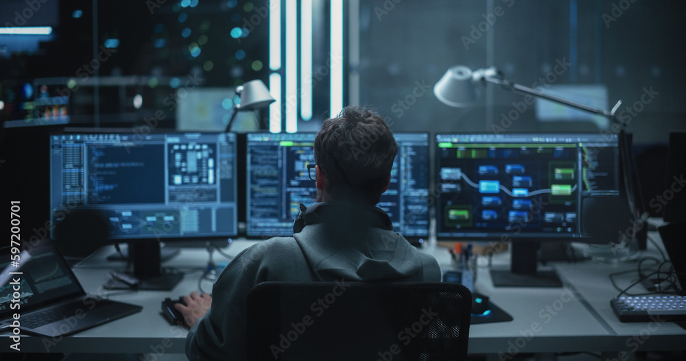 Poster Lone Hacker Breaks Into Government Data Servers and Infects Their System with an Exploit Software. His Hideout Place is in Dark Technological Facility with Multiple Displays. Shot from the Back