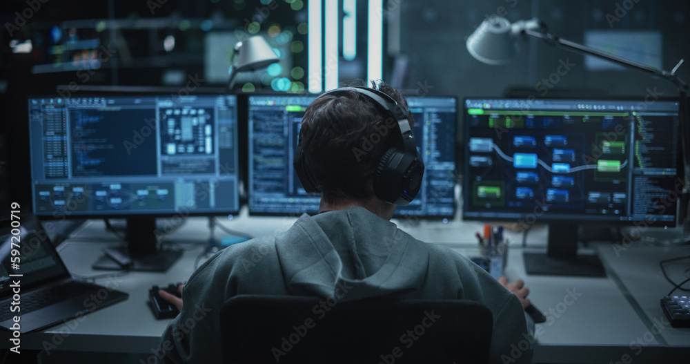Poster System Administrator Working in a Dark Research Facility on a Computer with Multiple Displays. Software Developer in Casual Clothes Wearing Headphones and Updating Server System Database