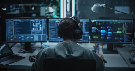 System Administrator Working in a Dark Research Facility on a Computer with Multiple Displays....