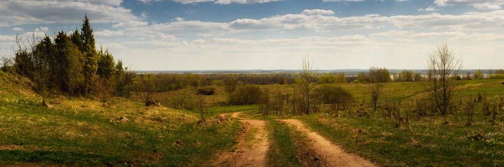 country dirt road through a hilly field. spring landscape. widescreen panoramic side view - obrazy, fototapety, plakaty