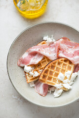 Beige plate with waffles, bacon and feta, vertical shot on a light-beige stone background, elevated view, middle close-up