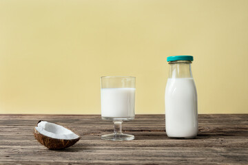 A glass and a bottle with vegan coconut milk and a piece of coconut on a wooden table, alternative and healthy milk concept