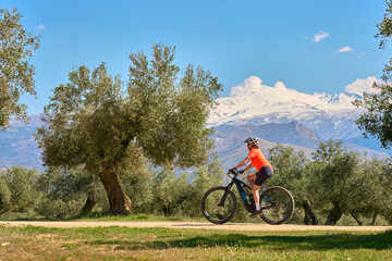 Fototapeta na wymiar nice, active senior woman cycling with her electric mountain bike below the snow covered mountains of the Spanish Sierra Nevada, near Granada, Andalusia, Spain