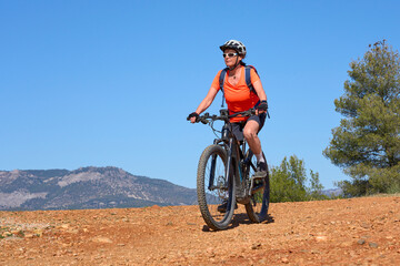 Fototapeta na wymiar nice, active senior woman riding her electric mountain bike in the pine tree forests near Granada, Andalusia, Spain
