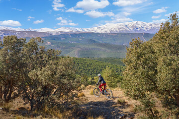 nice, active senior woman cycling with her electric mountain bike below the snow covered mountains...