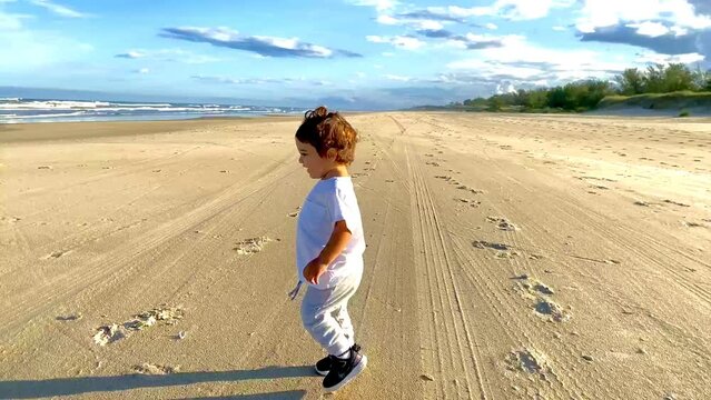 Small child playing in the sand on a deserted beach at the end of the day in a sunset with waves, dunes and nature. Mention children's play outdoors and its importance in motor and mental health.