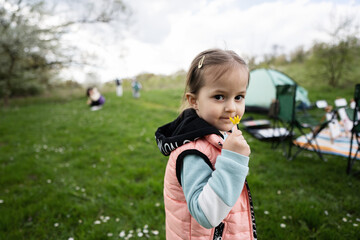 Baby girl sniffs a yellow flower on spring meadow.