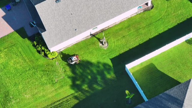 Top view of lawn mowing professional service worker cutting grass in summer with a lawn mower vehicle. Landscaping of rural home backyard