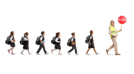 Full length profile shot of schoolchildren walking behind a teacher with stop traffic sign