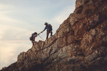 Hiking team hand to hand helping each other while climbing up on the mountain rock adventure travel...