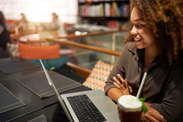 portrait young black afro young woman looking using her laptop smiling grabbing her hair in a cafe or library 