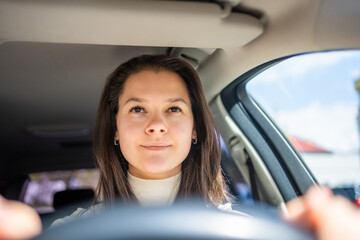 Fototapeta na wymiar Happy woman driving a car and smiling. Cute young success happy brunette woman is driving a car. Portrait of happy female driver steering car.