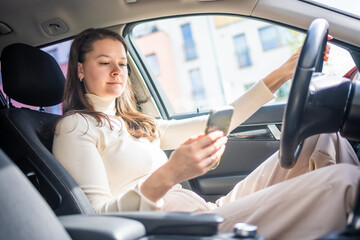Fototapeta na wymiar Young woman sitting in car and using smart phone, business woman busy driving