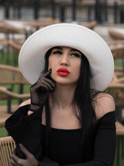 A woman in a black dress, at a table in a summer cafe in a white hat. One