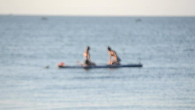 Two girls sit on SUP boards with oars on water surface of sea waves on sunny summer day. Women on SUP boards in sea in morning. Concept of leisure relaxation sport entertainment. Blurred background