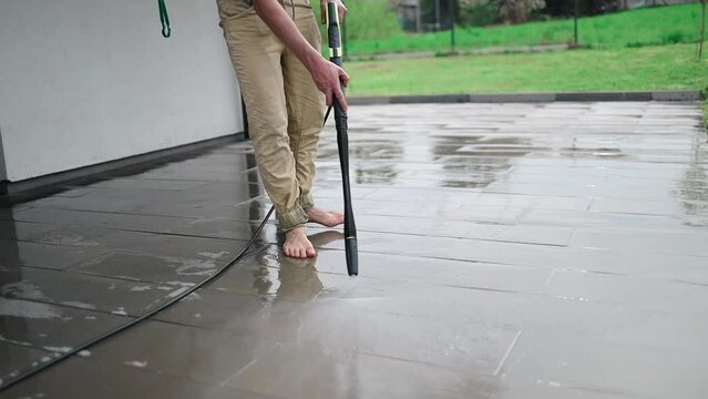 Cleaning stone slabs on patio with the high-pressure cleaner. Person worker cleaning the outdoors floor. 