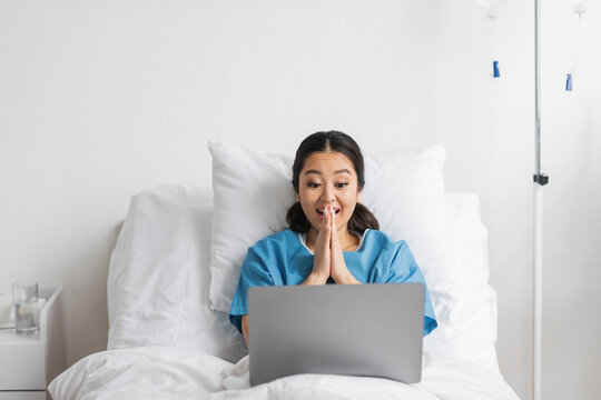 Excited Asian Woman Gesturing During Video Call On Laptop In Hospital Ward.