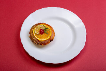 Cheese cake with marmalade and lime and orange slices in a white plate on a red background