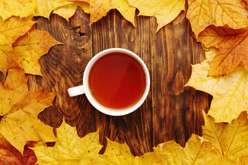 autumn leaves with a cup of tea or coffee on a wooden background with copy space