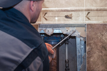 Handyman fixing a water pipe. Plumbing repair in a broken wall of a house.