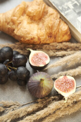 Gold autumn. Croissant, dark grapes, book and figs on the grey table