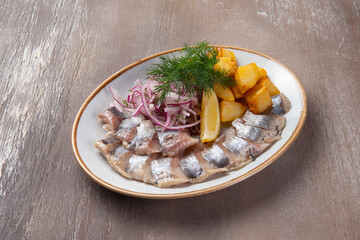 Herring fillet potato wedges in a plate on a brown background.