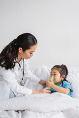 young doctor helping asian girl breathing in oxygen mask on bed in hospital ward.