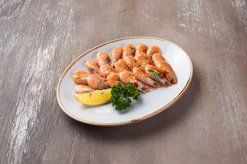 Cooked shrimp and lemon in a plate on a brown background.
