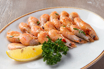 Cooked shrimp and lemon in a plate on a brown background.