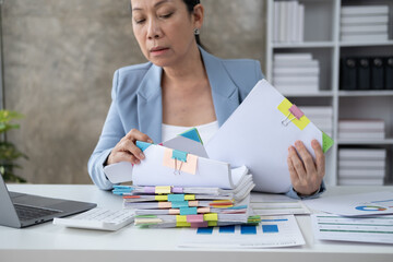 Smart senior businesswoman working in her office room with laptop computer and stack of papers.