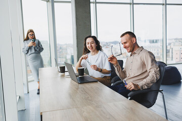 Workflow in an office with large windows, colleagues working on a new project using a portable laptop. Modern office with employees.